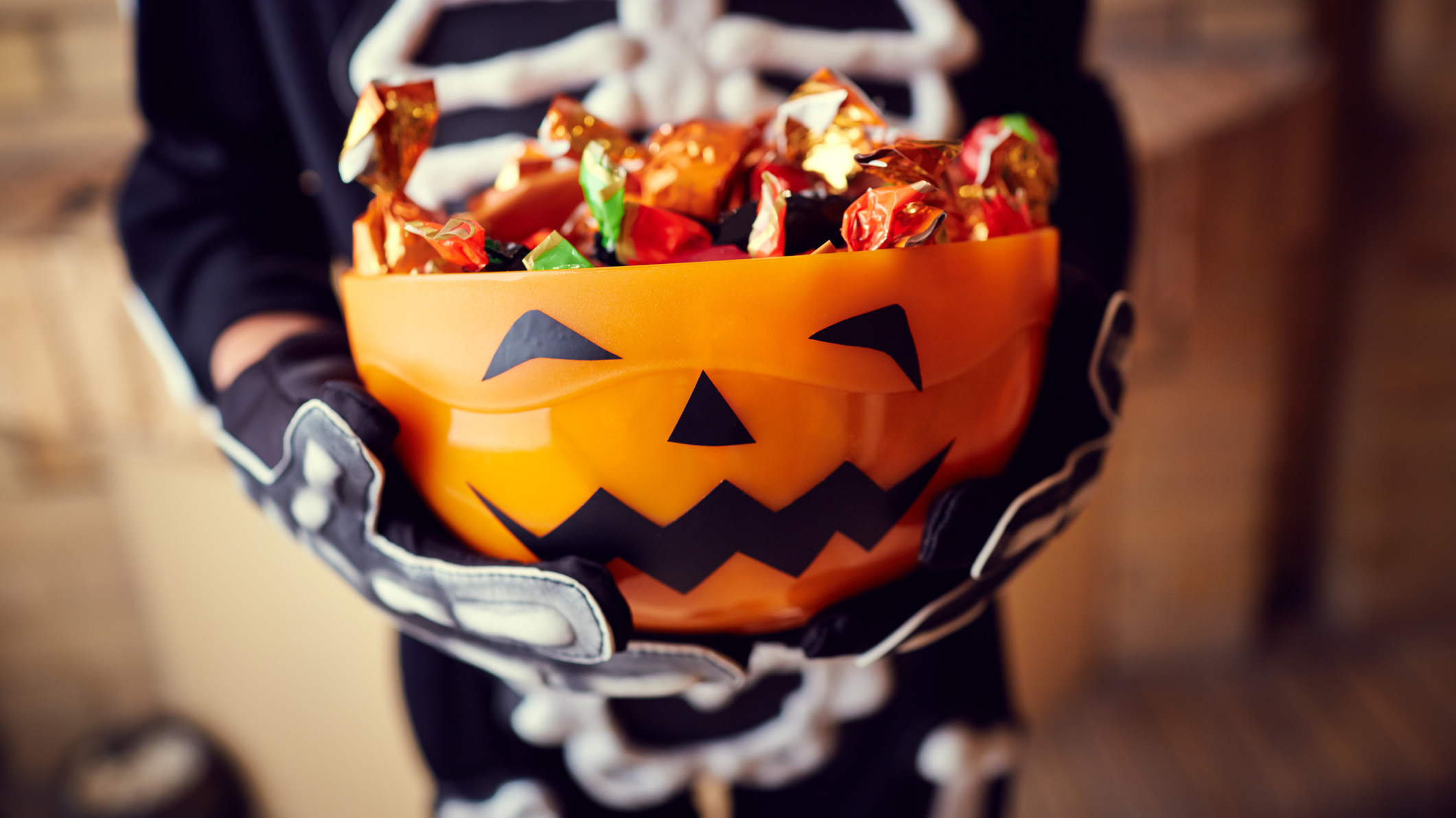 Child in skeleton costume holding a Halloween pumpkin candy basket